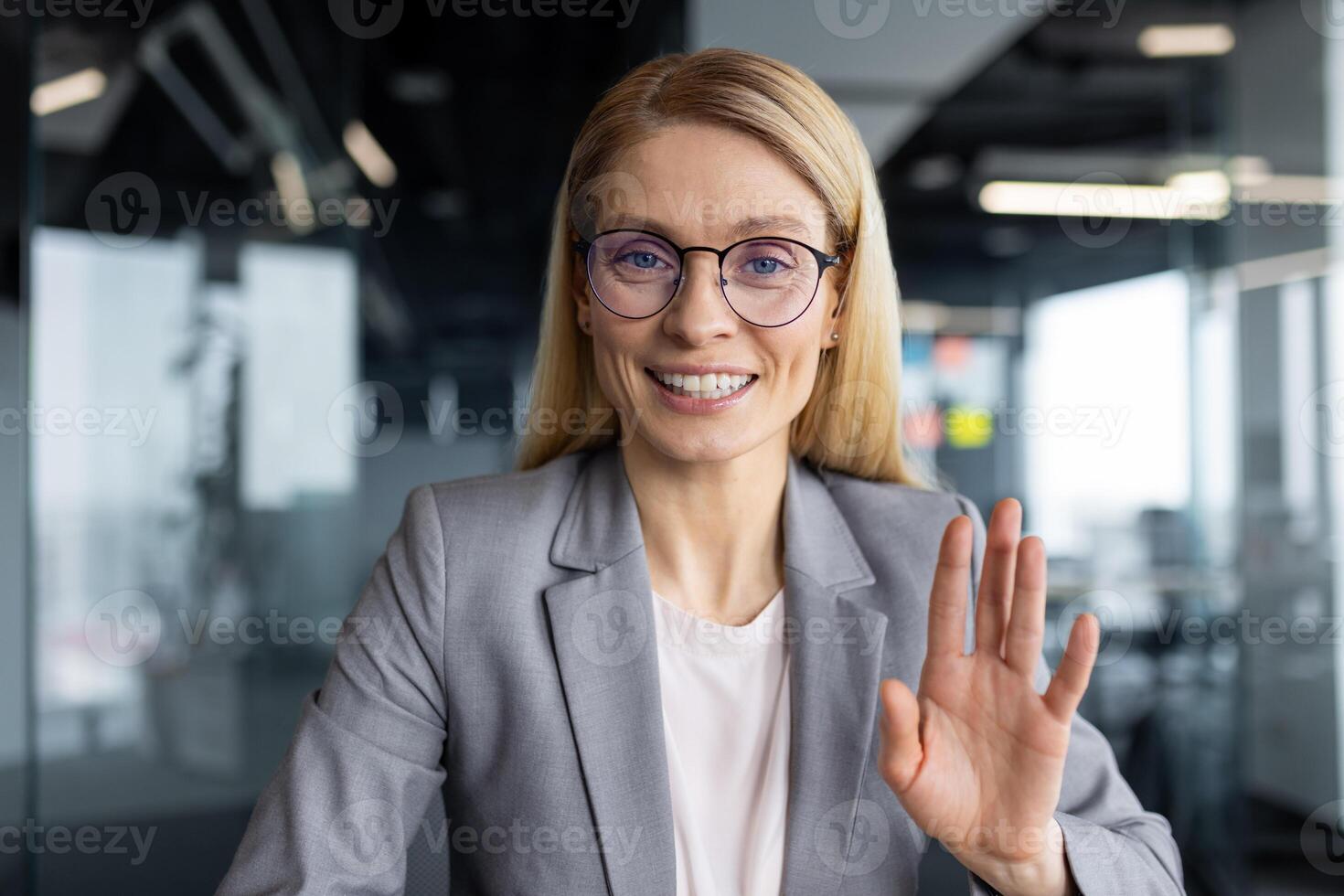 Webcam view of successful joyful businesswoman talking to colleagues and partners using laptop and call. Woman looking at camera while sitting inside office at workplace, online meeting. photo