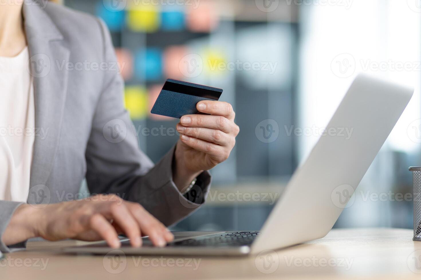 A woman is shopping online using her credit card and laptop in the office, making secure purchases from the comfort of her desk photo