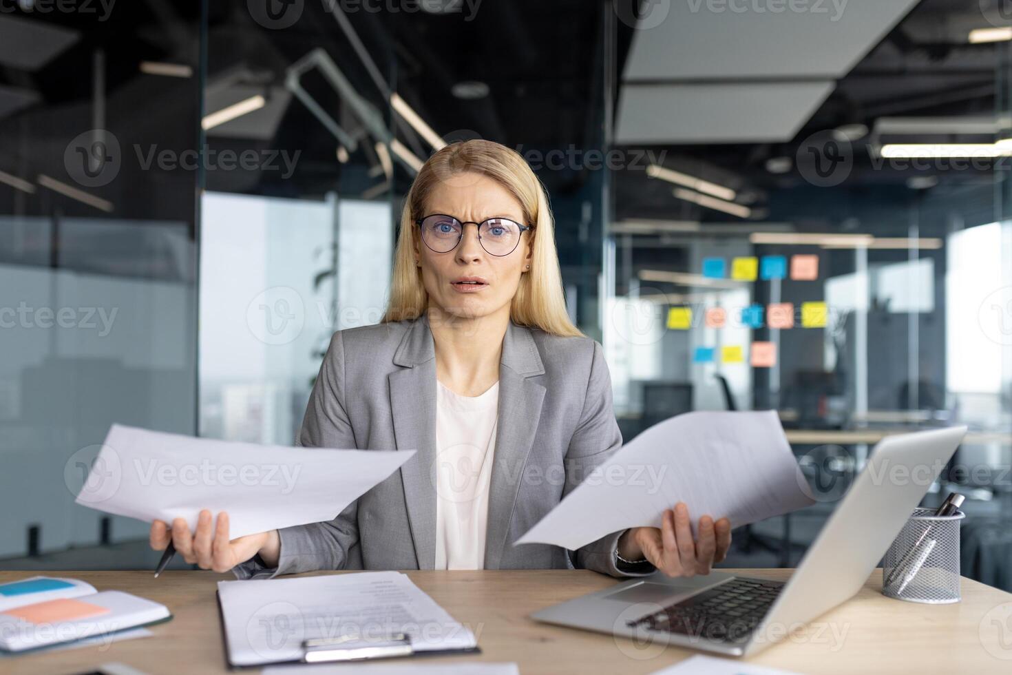 A professional woman appears perplexed while holding documents in a modern office setting. She seems surprised with the information. photo