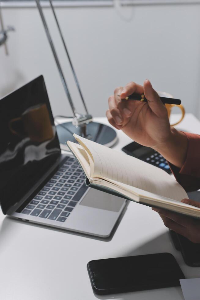 A person writing in a notebook at a desk with a laptop and a pen photo