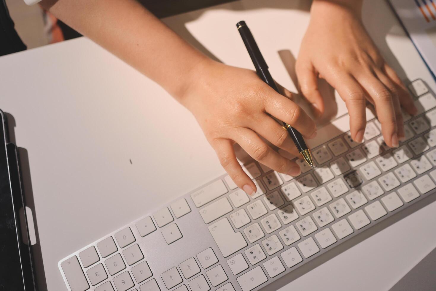 A person's hands on a keyboard and a pen photo