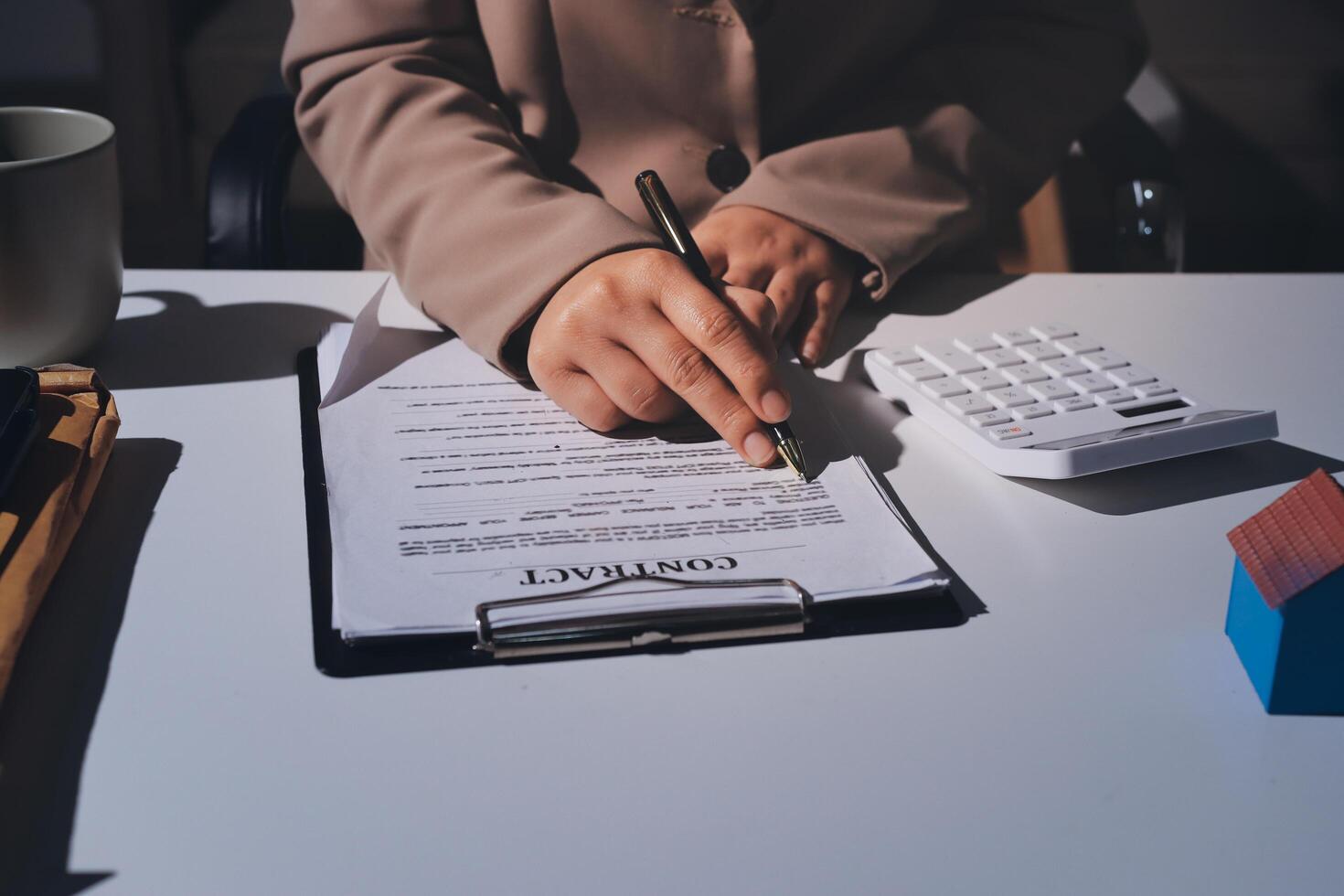 A woman signing a contract on a desk with a calculator and house model photo