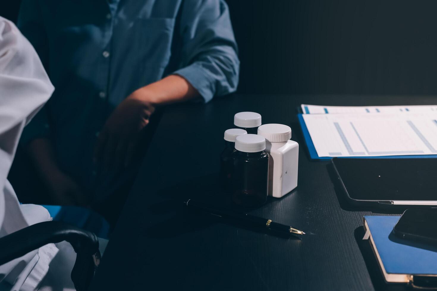 A doctor is sitting at a desk with a laptop and a bottle of pills photo