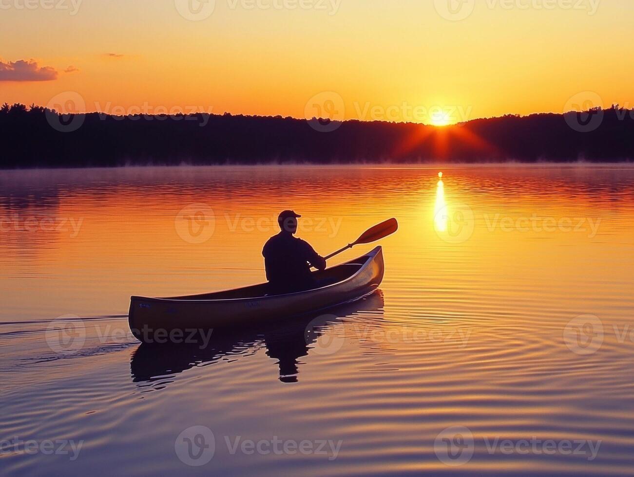 Canoeist paddles at sunset over calm lake waters photo