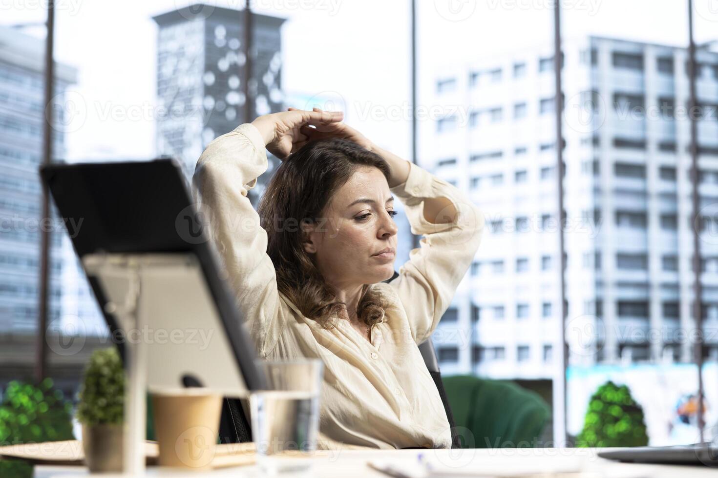 Chill pleased female entrepreneur takes a break in her CEO chair, resting in her high end corporation workspace. Skilled empowered leader relaxing after solving business tasks. photo
