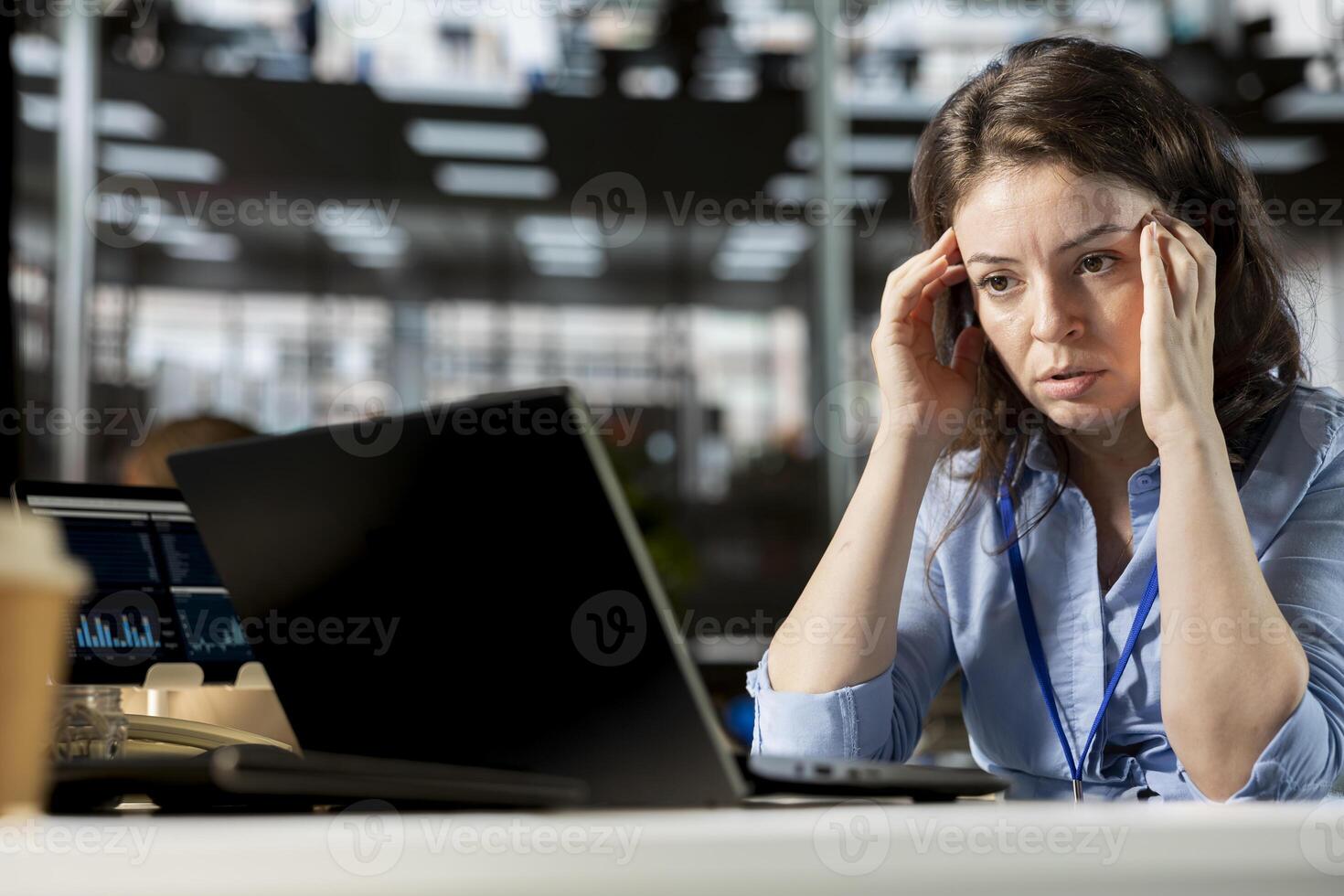 Sick company worker struggling at the office with a serious headache, exhaustion and burnout after working under pressure. Unwell woman dealing with a migraine, job discomfort. photo