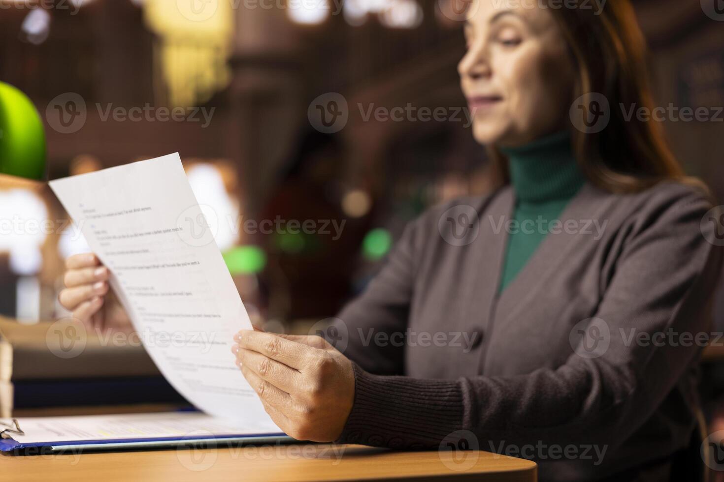 Aged focused woman in a public library studying educational materials and reading, representing preparation required for coursework and school exams. Learning from archived files. Close up. photo