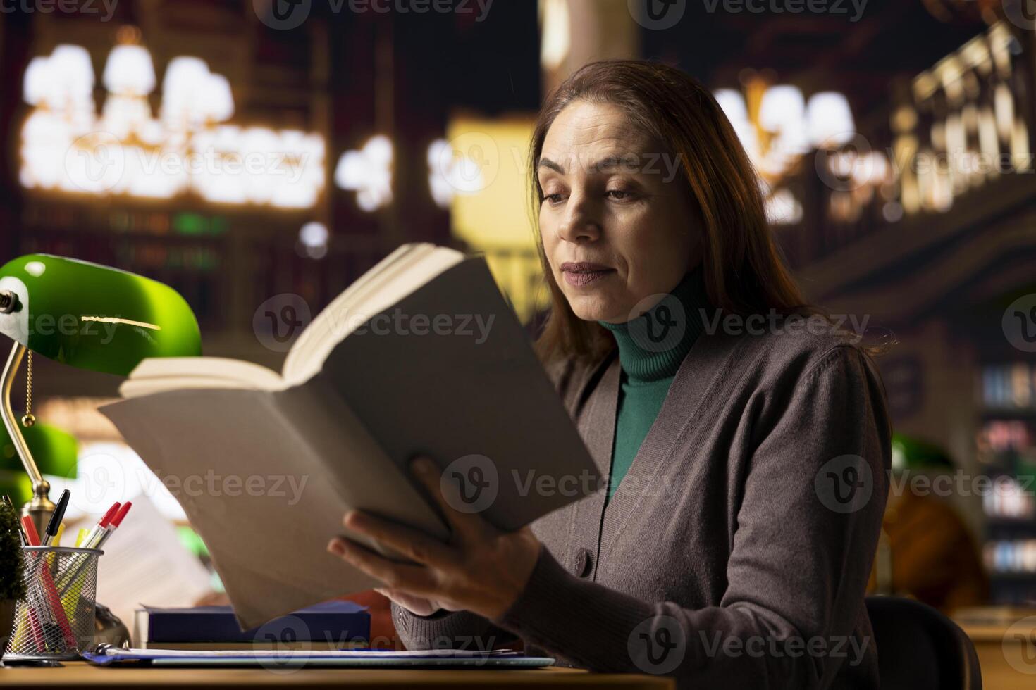 Mature female student in a work room surrounded by books and documents, preparing for a master dissertation and researching academic materials at the campus library. Higher education. photo