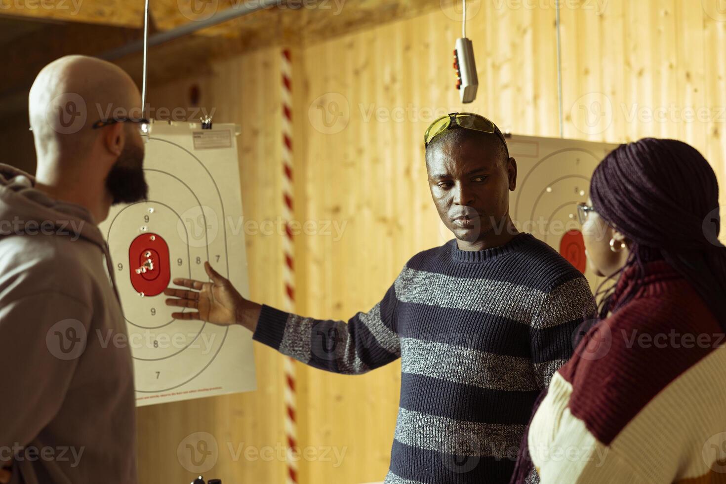 Shooting range safety specialist ensuring clients are operating weapons safely, explaining gun holding etiquette. Firing range gallery worker discusses rules with clients, teaching how to use firearms photo