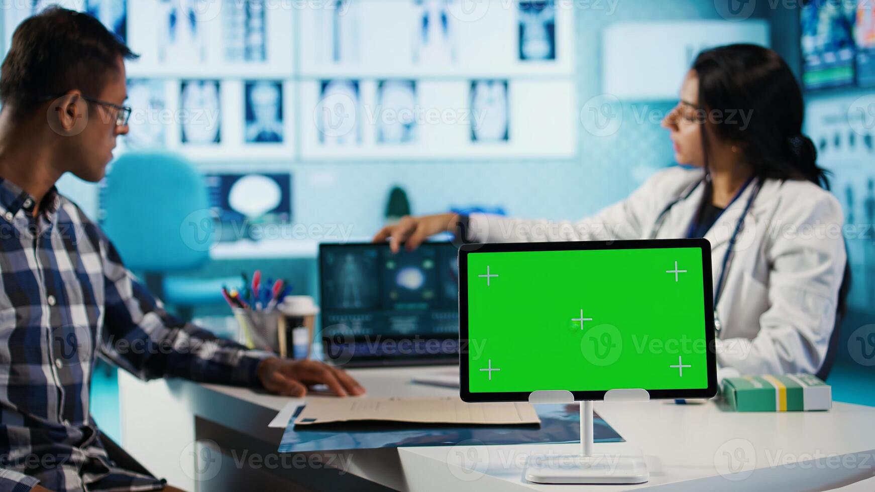 Female general practitioner and patient looking at green screen on tablet, recommending pills and drugs during check up. Indian people discussing about diagnostic report and remedy. Camera B. photo