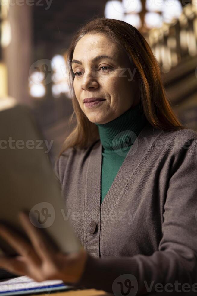 Mature university student preparing her thesis in a campus library study room, reading a book to collect academic information. Ambition and determination to complete a college degree. photo