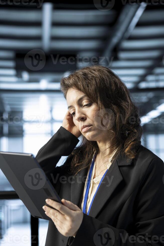 Computer scientist in data center with tablet integrating automation tools, running predictive maintenance routines. Woman ensuring continuous uptime of server room, managing data flows with device photo