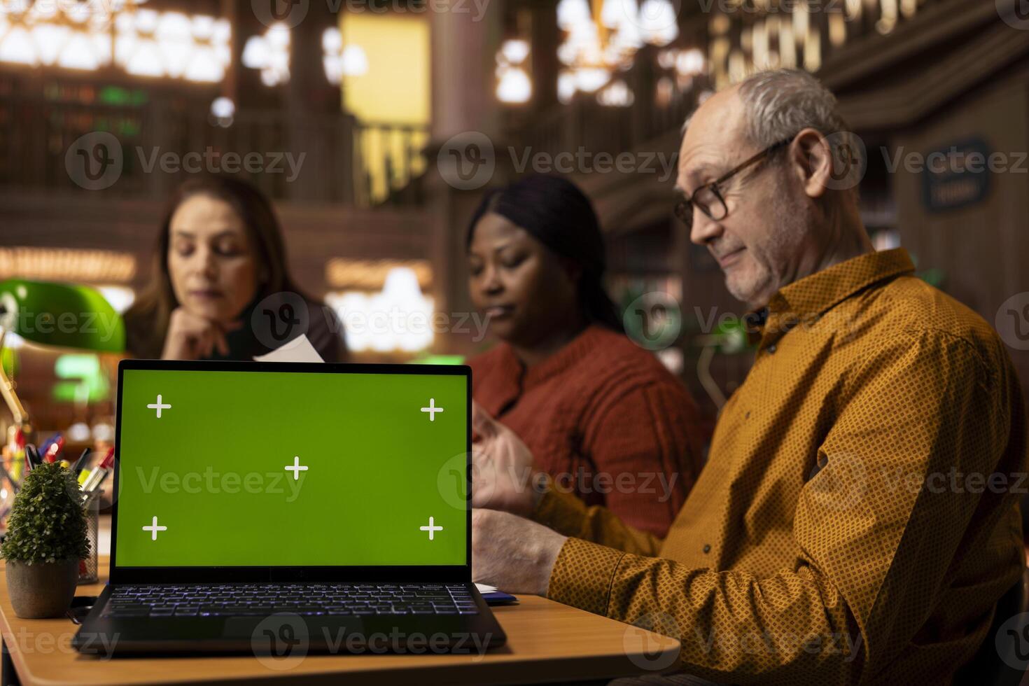 Focused group of university students read next to a green screen device, diverse people working on their thesis citations and documents. Analyzing coursework in a peaceful library. photo