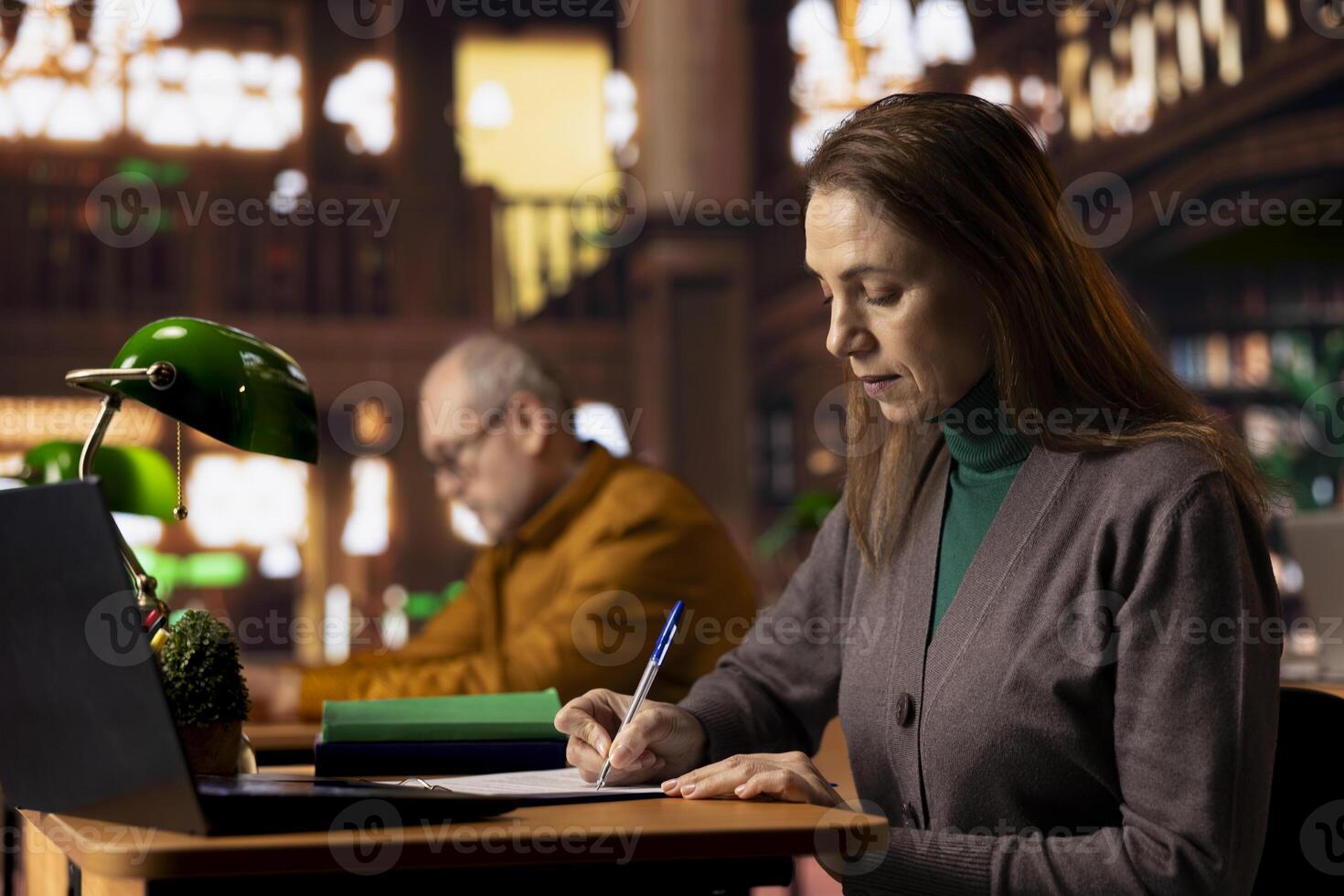 Mature female pupil writing class notes on clipboard files at the library, studying and reading at a college campus. Woman symbolizing preparation for her diploma thesis, intellect. photo