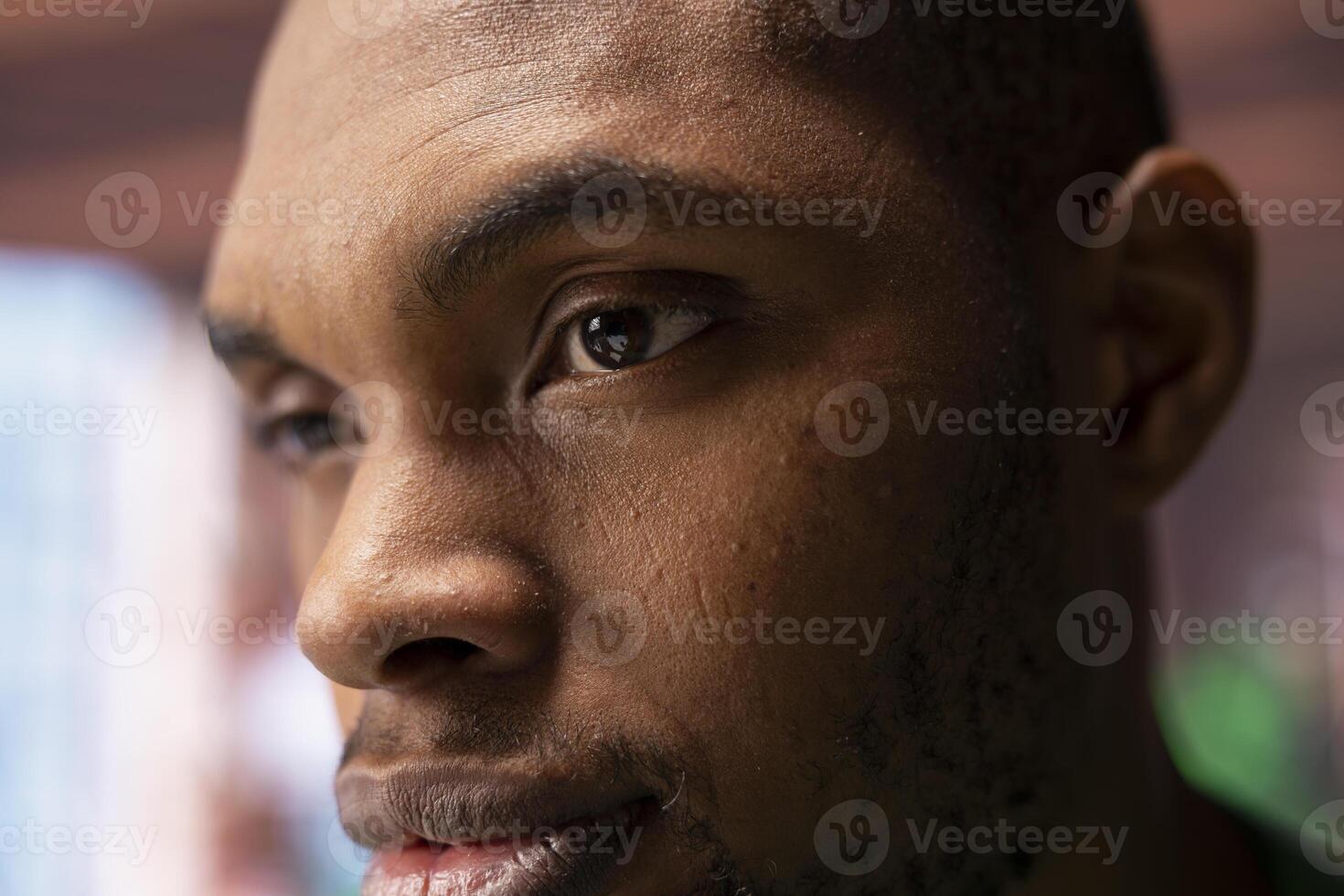 Focus on man eyes with pensive reflective look doing ruminating in apartment. African american person with focused expression lost in deep thoughts, extreme close up shot photo