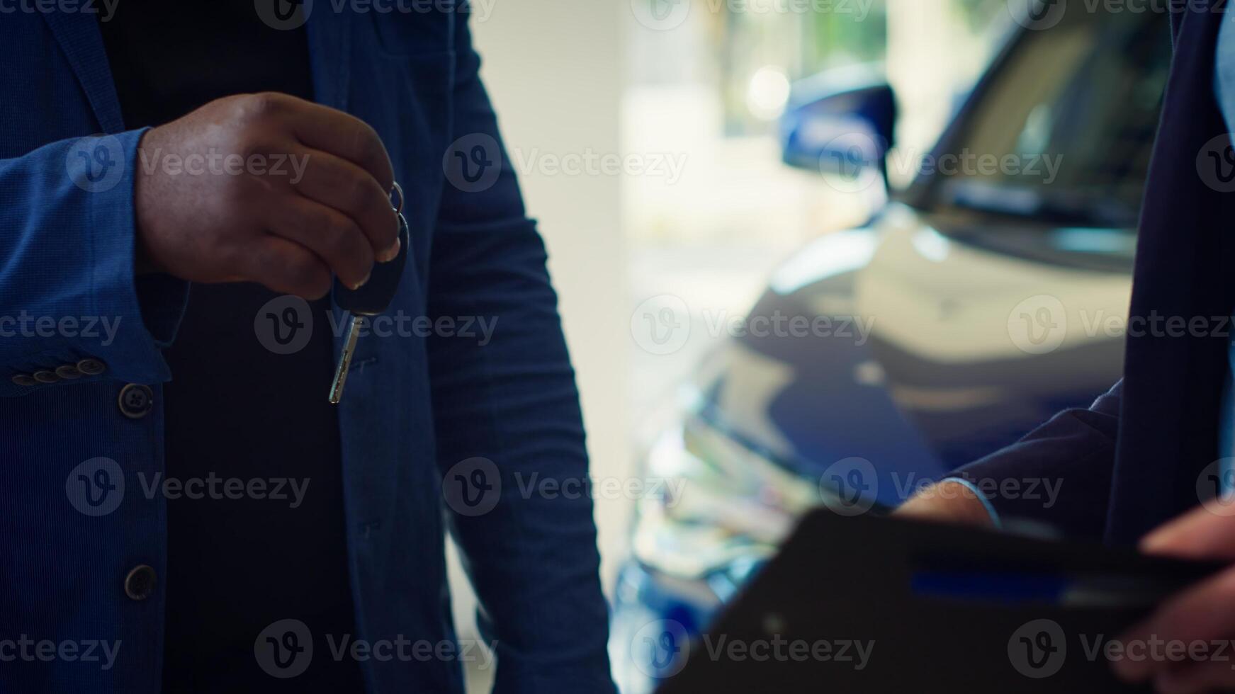 Showroom dealer completes paperwork after selling vehicle, shaking hands with buyer and offering car keys. Salesman in dealership signing contract with man, reaching agreement, camera A close up photo