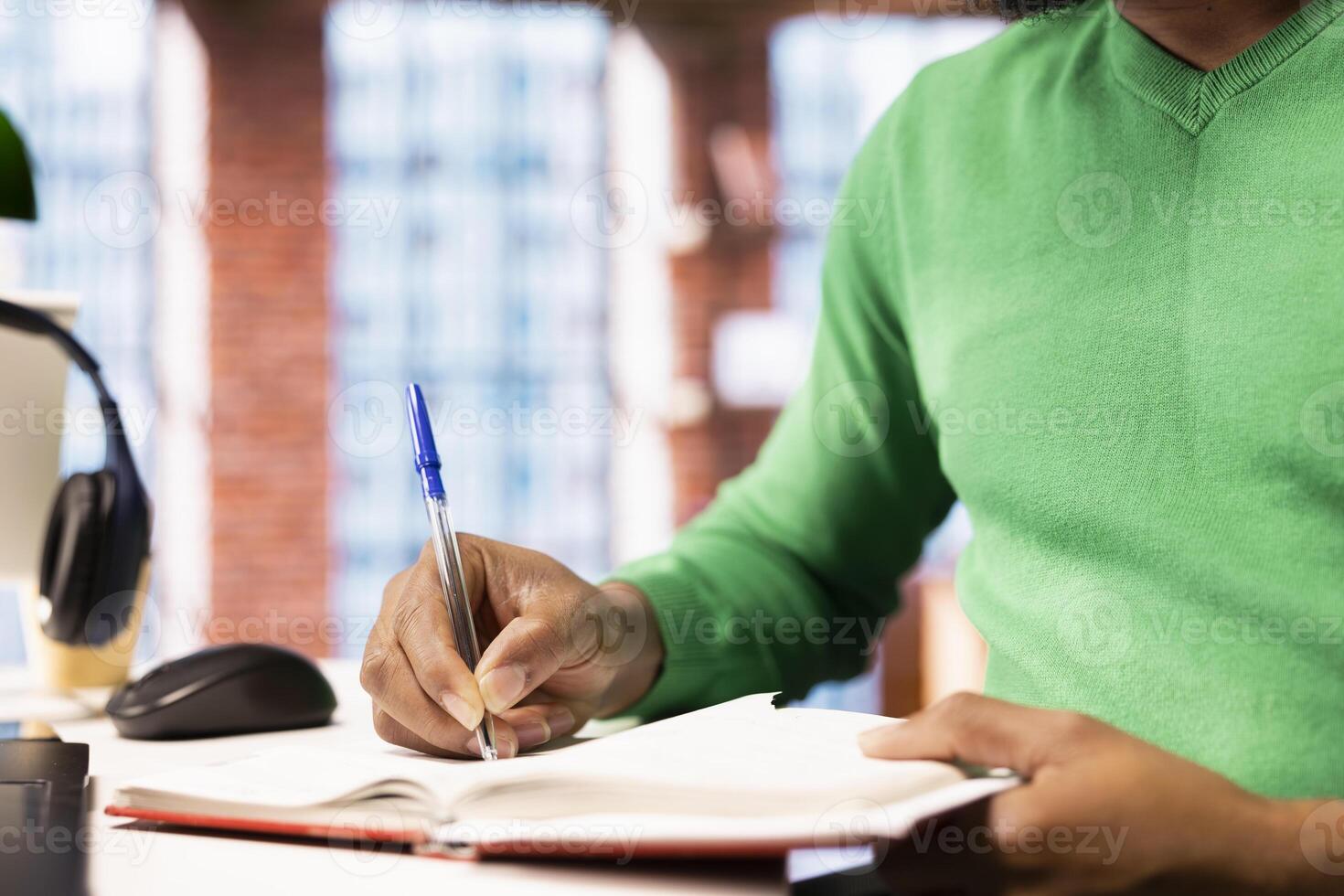 Person preparing for school exam, practicing on notepad at home office desk, close up. African american student doing homework, writing down info with pen, researching for college tests photo