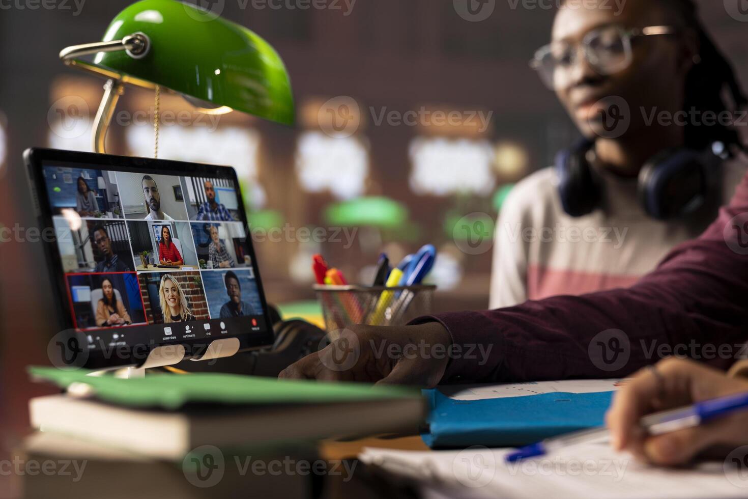 Group of diverse pupils engaging in an online course discussion via call, participating at the remote class seminar from the campus library. Young people takes notes from academic tutor. photo