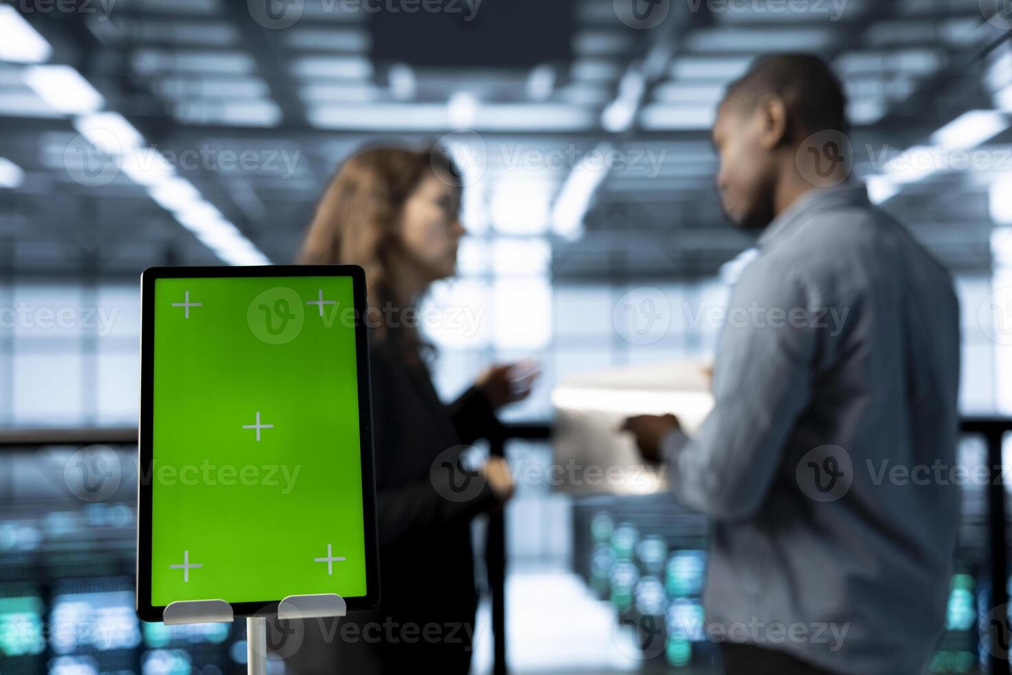 Close up of mockup tablet next to workers in data center using automation tools. Focus on isolated screen tablet in front of technicians in blurry background ensuring continuous uptime of server farm photo