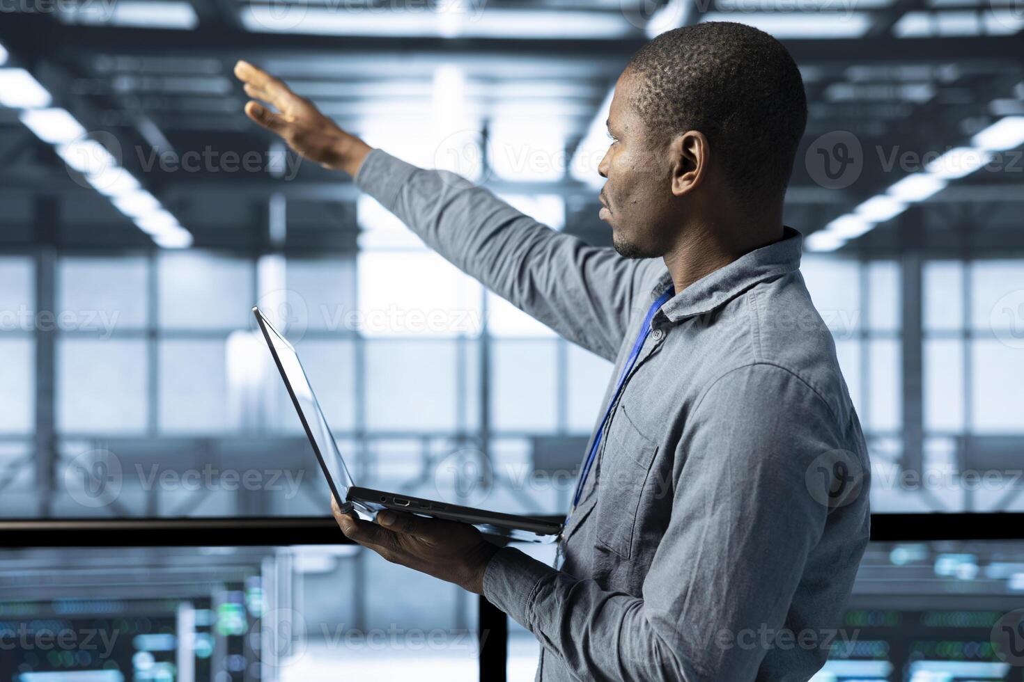 Technician holding laptop, looking around data center, managing server virtualization, finetuning network protocols, verifying high availability configurations, enforcing advanced security measures photo