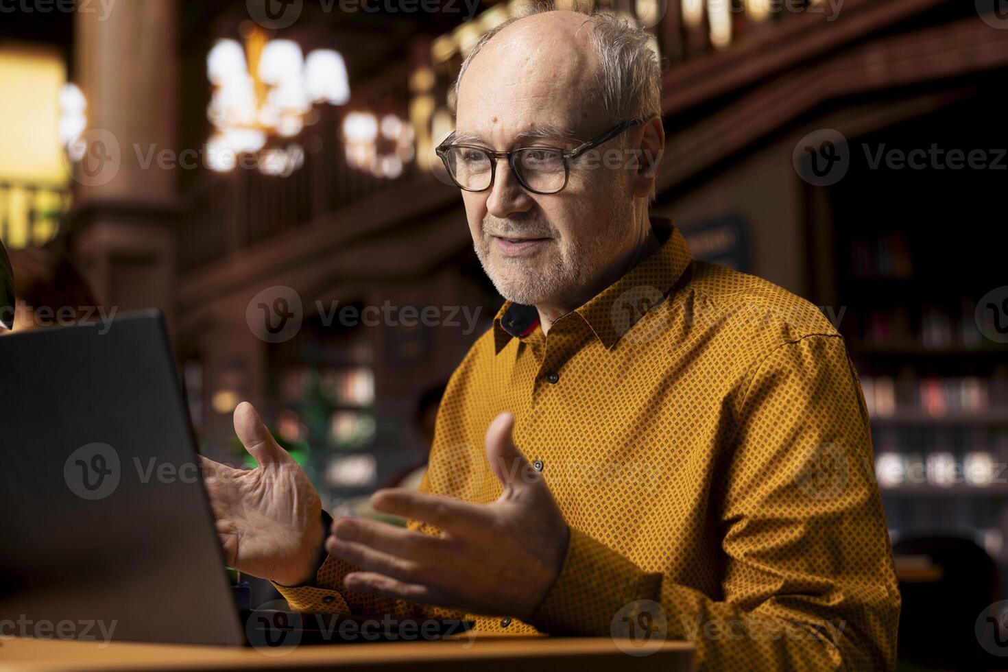Senior man involved in a remote classroom experience via online platform, using wireless internet to study a university course and chatting with his teacher. Reviewing project materials. photo
