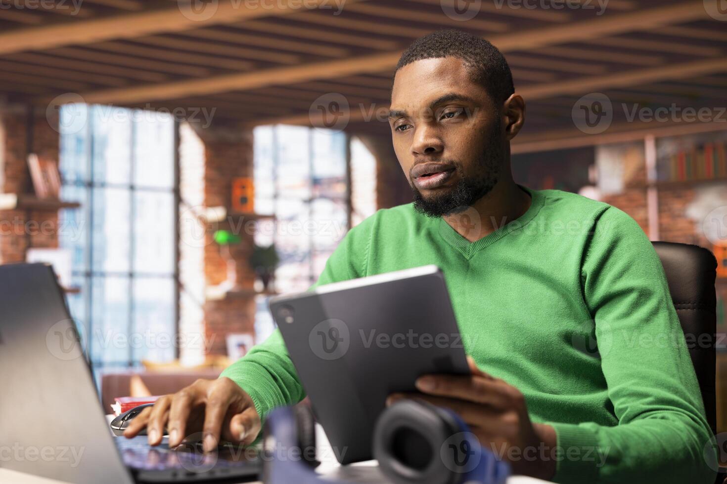 Remote worker using laptop and tablet in home office to write emails. Freelancer using digital devices, composing documents in order to deliver finalized project paperwork photo