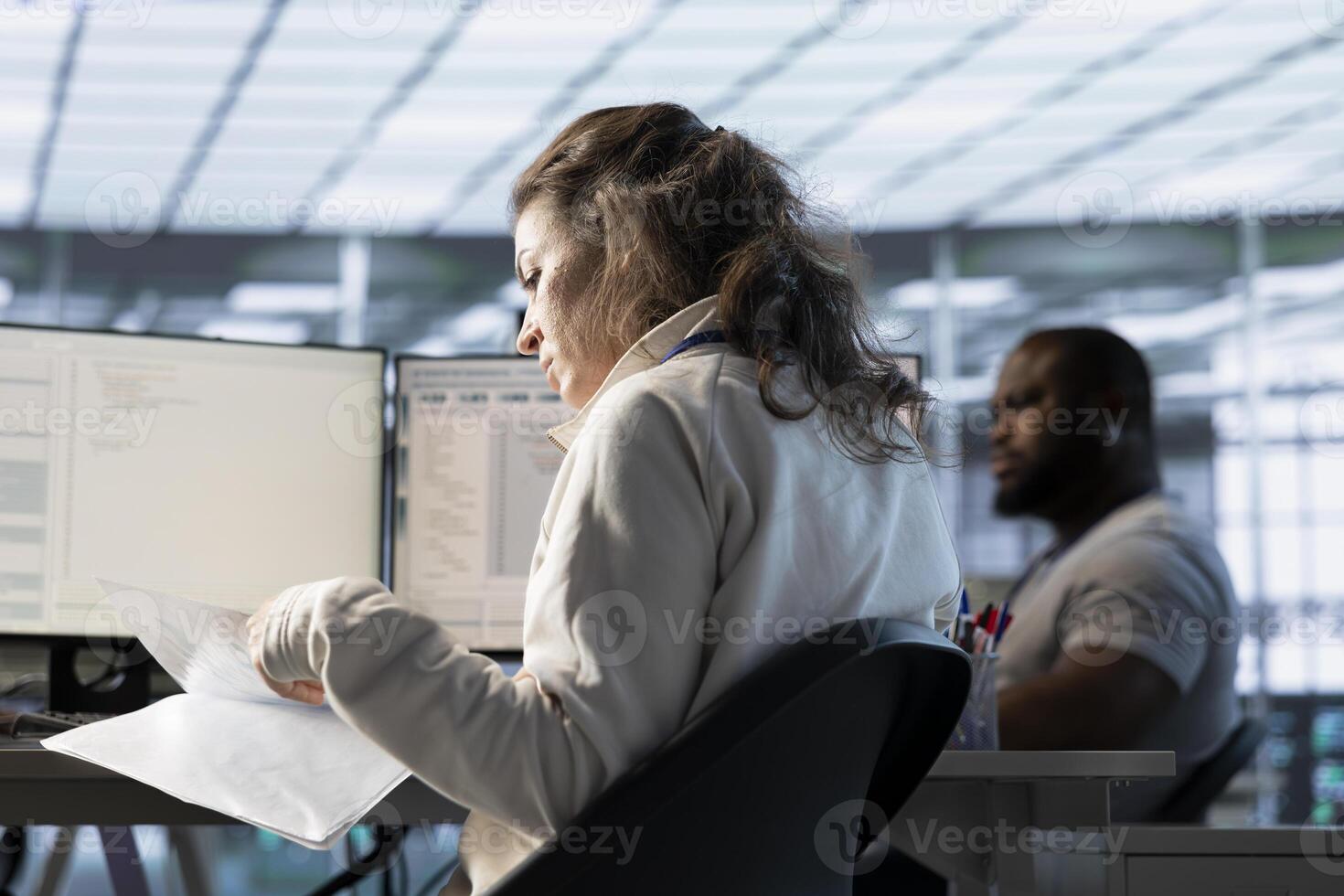 Woman overseeing server room, reading documentation paperwork, troubleshooting hardware. Supervisor doing inspection in server hub, reading technical files at computer desk photo