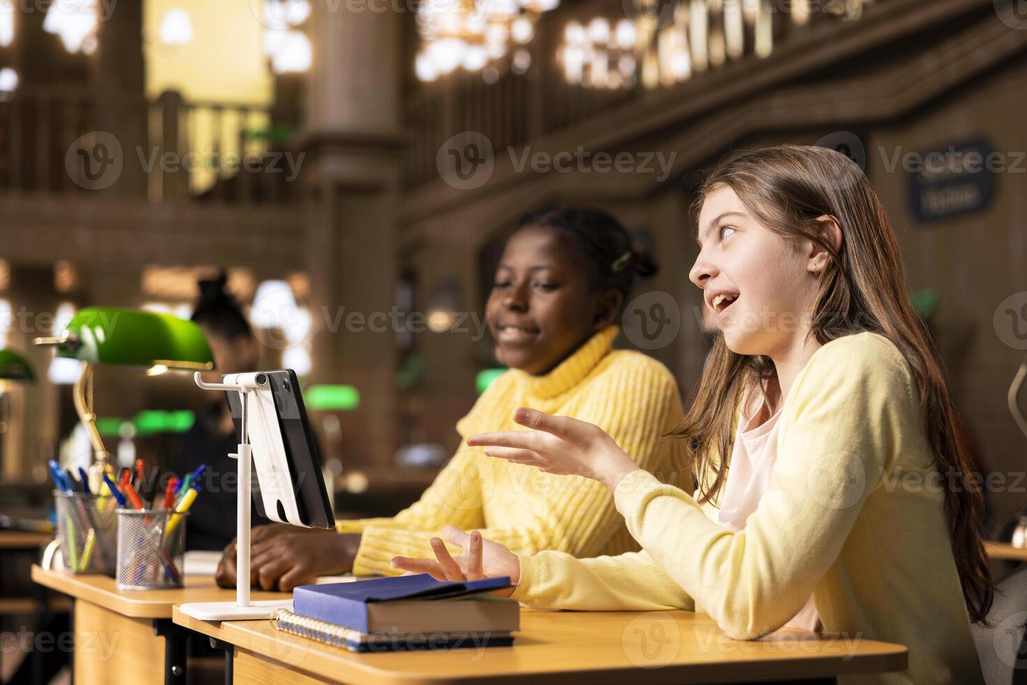 Girls participating in an online course at the library joining a live webinar with their teacher to complete a school project. Scholars working on an assignment via call lesson. photo