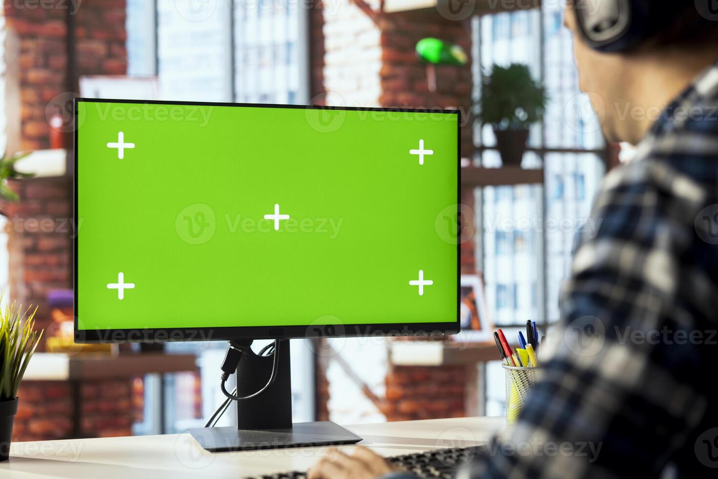 Worker listening music, analyzing data on green screen PC at desk, compiling analytical reports. Close up of employee wearing headphones using mockup computer, finishing project photo
