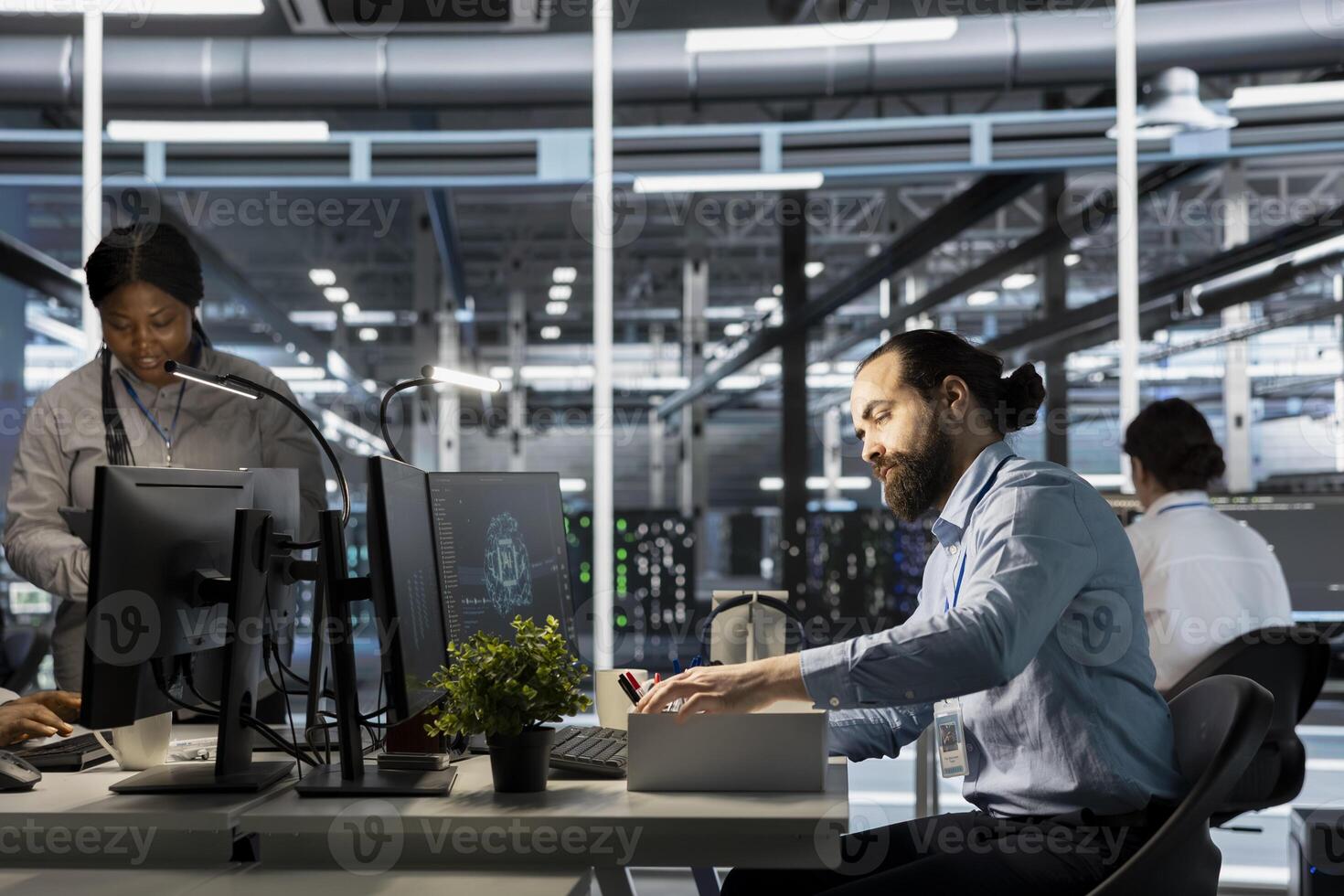 Upset engineer in data center packing personal items at workstation after being replaced by AI. Technician removing belongings from server hub workplace desk, fired by artificial intelligence photo