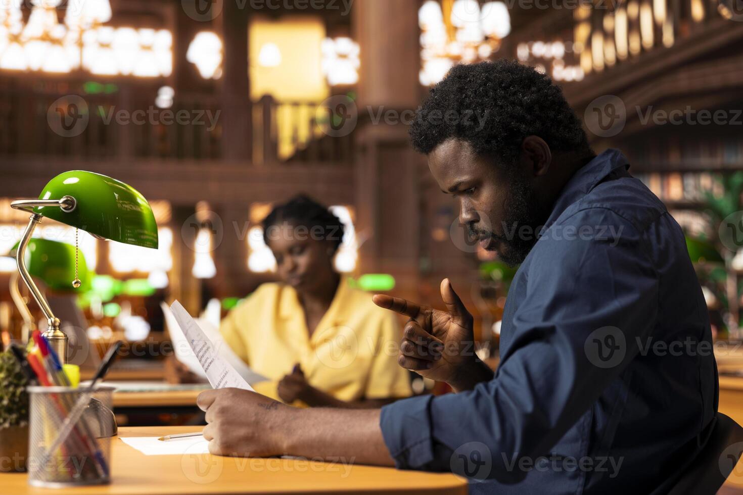 Ambitious university student researches academic topics in a library, using the campus study space to learn lessons and organize his course materials. Completing class notes for exams. photo