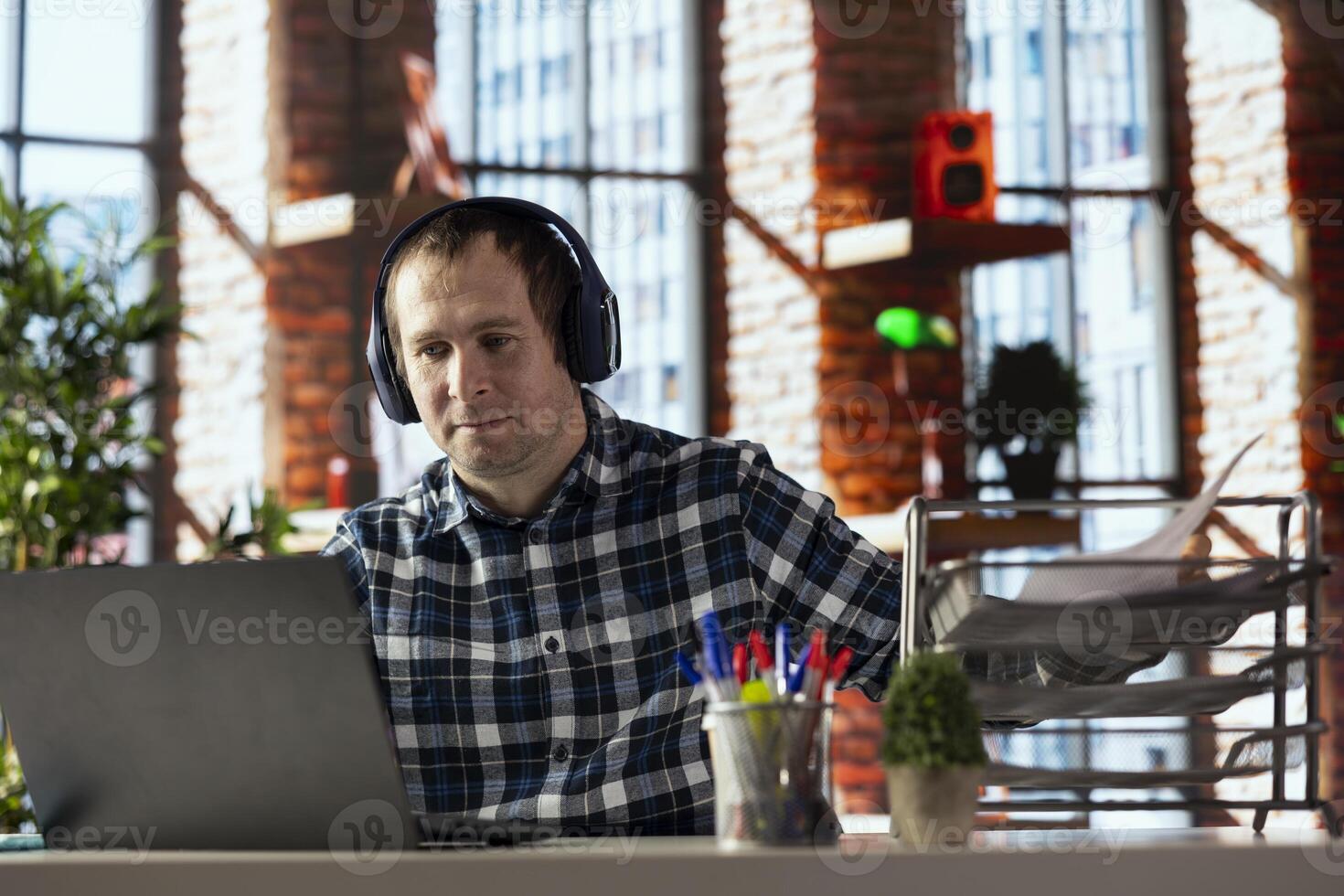 home office worker at desk using laptop, engaging in call, participating in virtual meeting with colleagues. Man discussing with coworkers during videoconference meeting, using headset photo