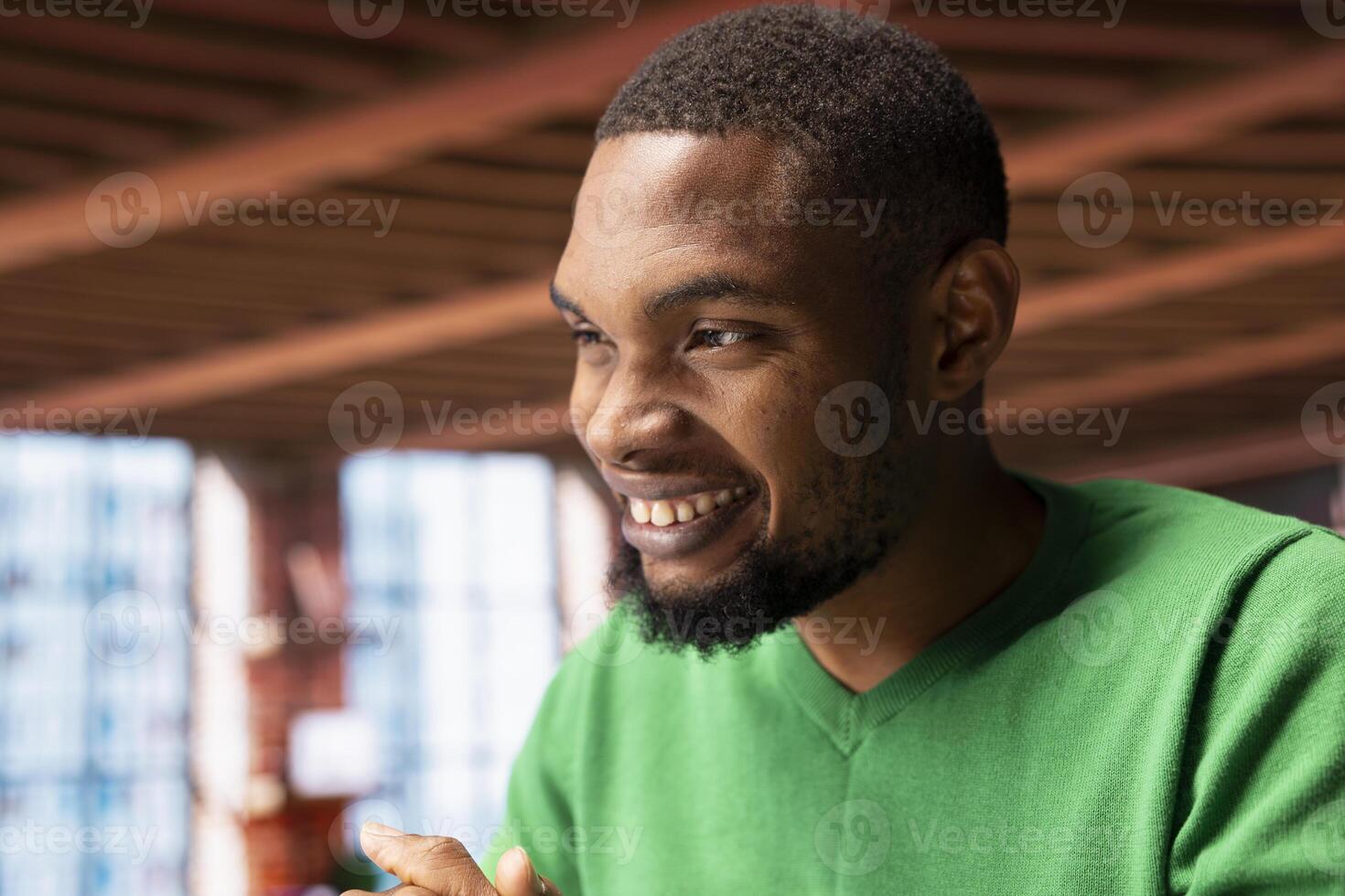 Joyous happy african american man in apartment smiling, looking pleased, enjoying leisure time. Jolly upbeat person sitting at home desk exulting, feeling satisfied, close up shot photo