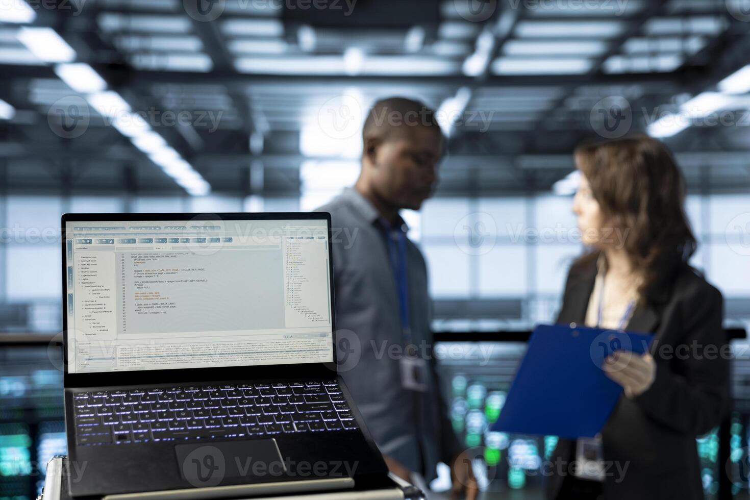 Close up of code lines on laptop screen in front of data center engineers checking documents. Focus on programming language on notebook display next to team of server farm admins reading paperwork photo