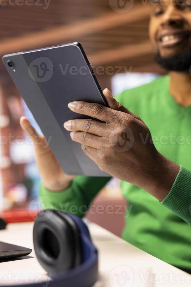 Man at home taking break from work to look at social media feed on tablet. Remote employee at work in apartment office pausing tasks to use social network application on device, close up photo