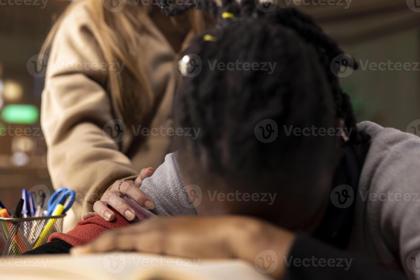 Colleague trying to wake up black student in the university library, girl falling asleep on her stack of borrowed books after studying all night. Sleepy overwhelmed person napping. Close up. photo