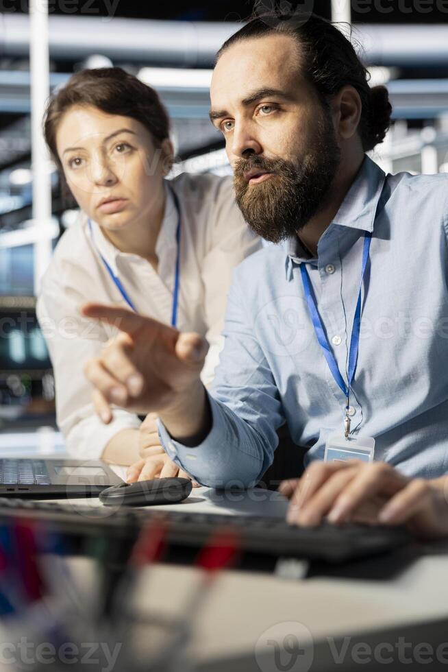 Programmers in data center workplace using computer, verifying firewall configurations. Teamworking colleagues doing brainstorming, performing equipment vulnerability scans in server hub using PC photo