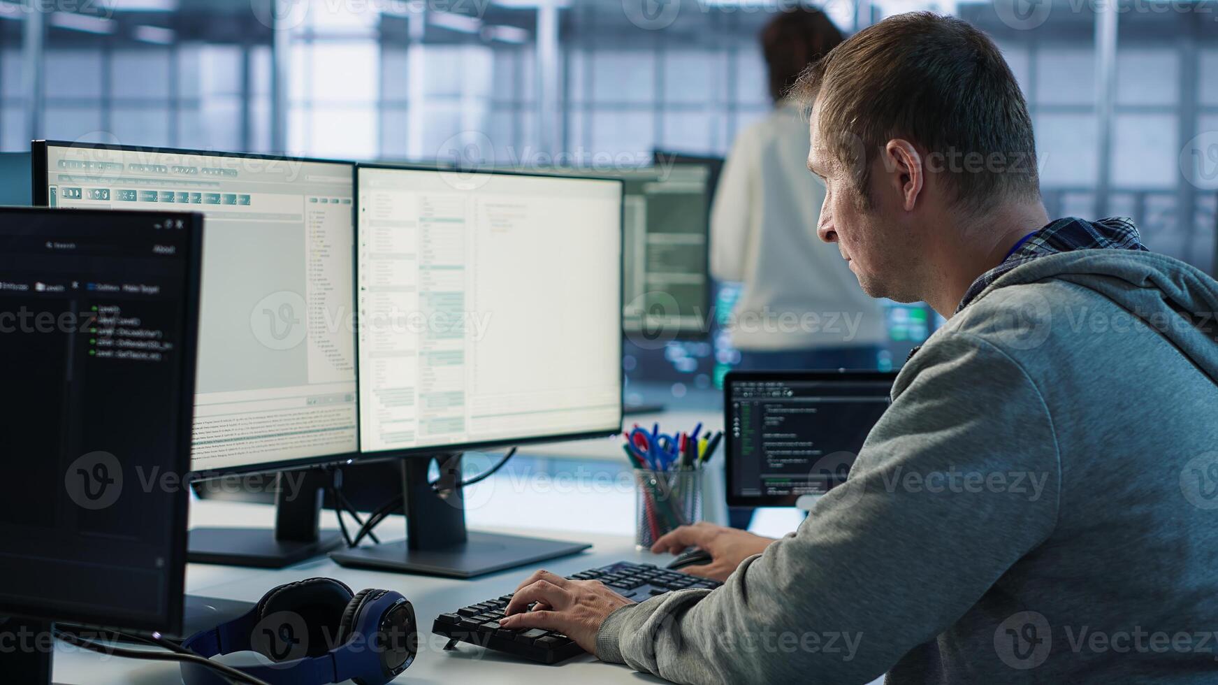 Engineer starting job shift in server hub used for processing vast amounts of data. IT programmer arriving at work in data center, sitting at PC desk, typing on keyboard, camera A photo