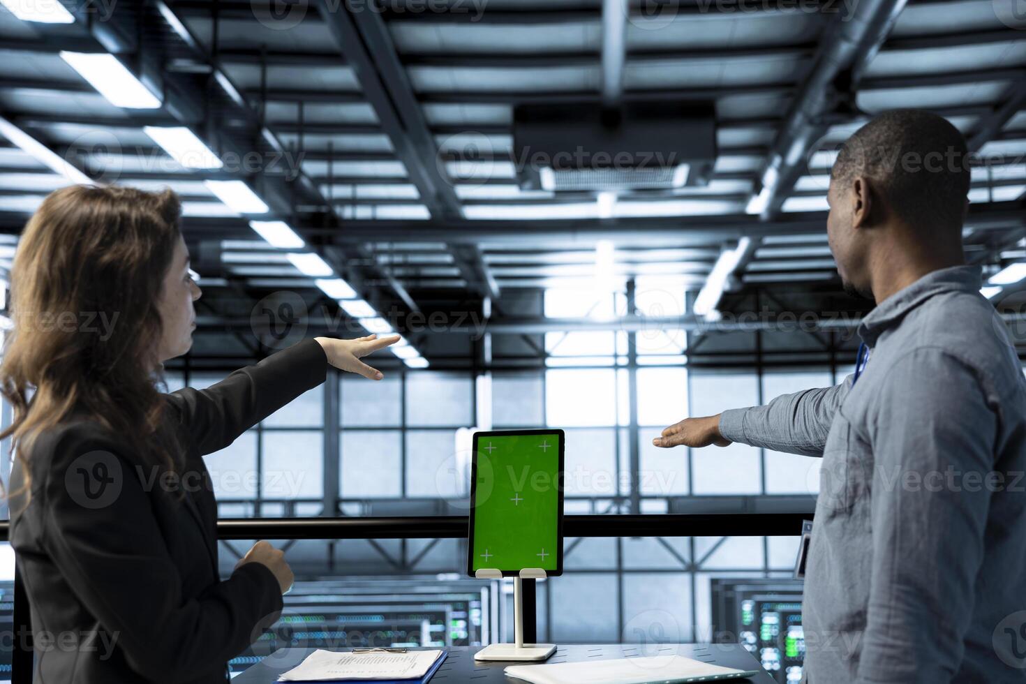 Computer scientists in data center use mockup tablet, inspecting server rigs, updating network topologies. Teamworking IT colleagues brainstorming, using chroma key device, ensuring stable operations photo