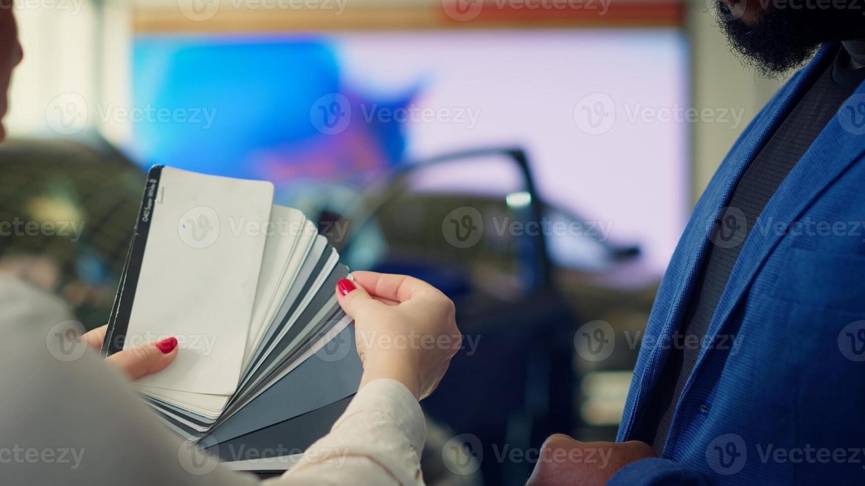Saleswoman in dealership talking with client, offering color swatch samples choice, trying to grasp their preferences for vehicle. Agent providing customer with color wheel tinting selection, camera A photo