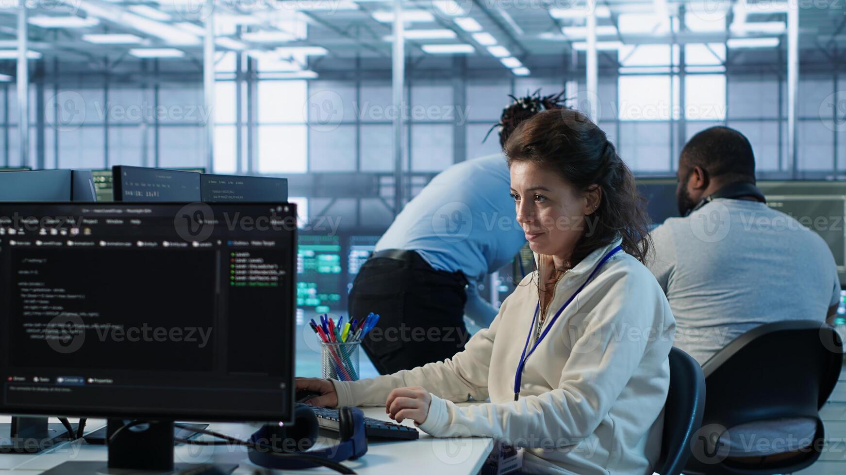 Upbeat computer scientist working in high tech server hub capable of processing vast amounts of data. Smiling woman at PC typing on keyboard, updating servers controlling network resources, camera A photo