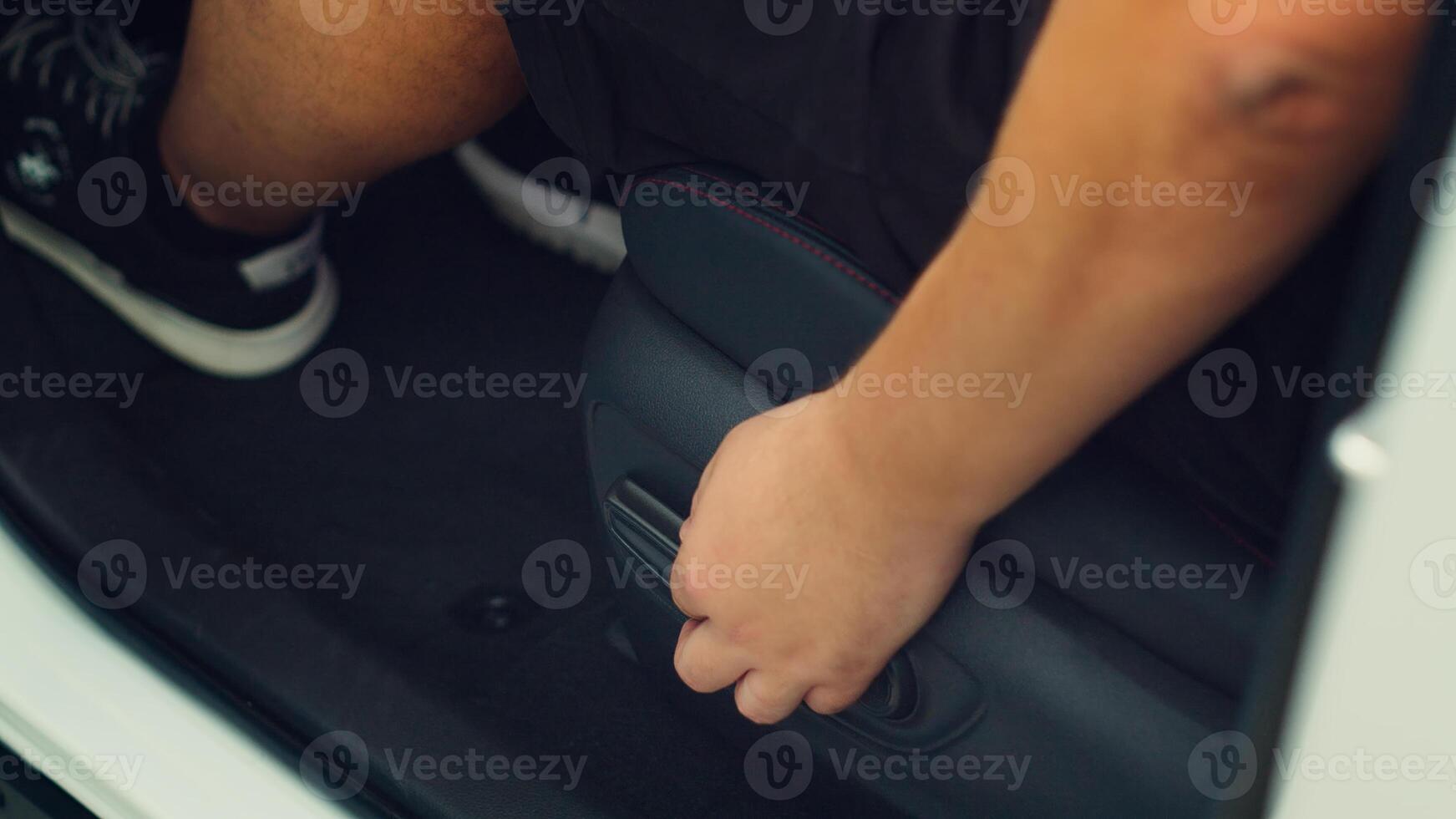 Close up of man in car pushing driver front seat forward using electric buttons. Person inside automobile moving vehicle chair closer to steering wheel using adjustment knobs photo