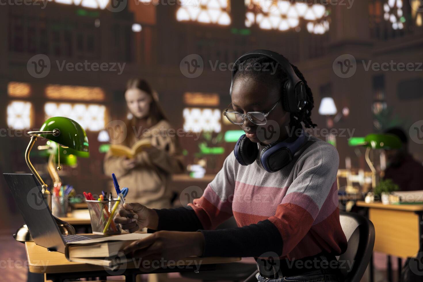 African american girl student listening to a podcast on headset and takes notes, using educational audio and materials for academic purposes. Scholar prepares for a class assignment. photo