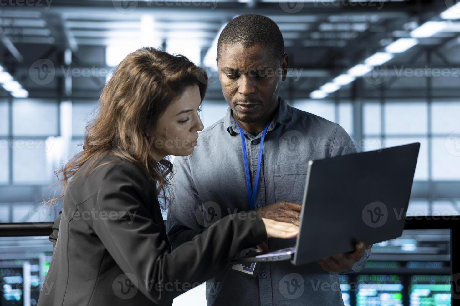 System administrators in data center automating routine maintenance tasks with laptop, executing diagnostic scripts. Server hub IT specialists talking, using notebook to adjust power settings photo