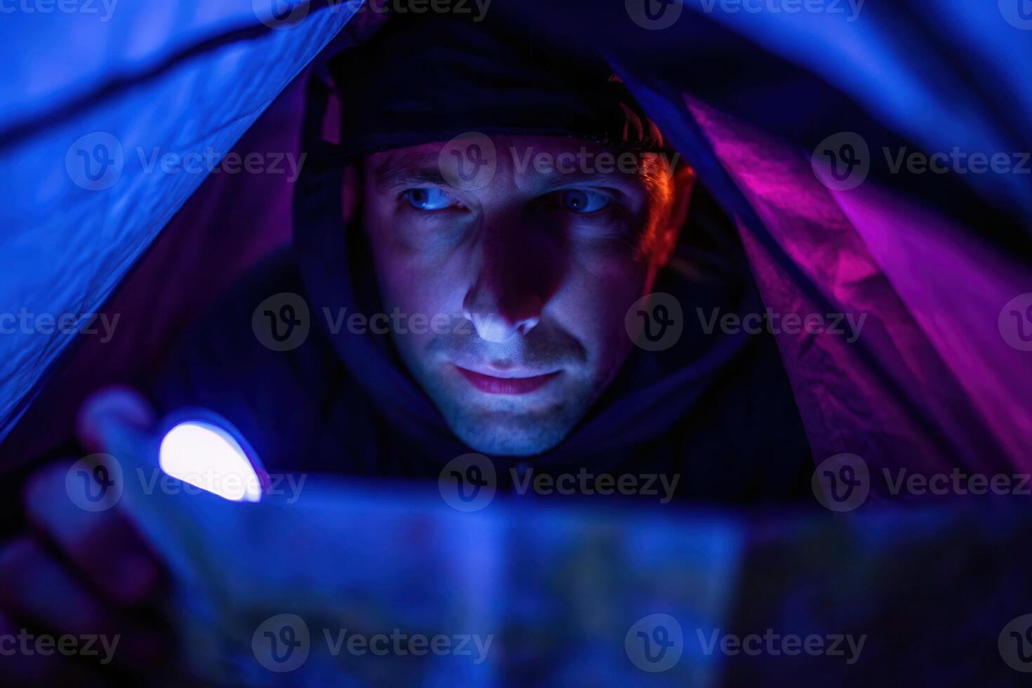 Backpacker reading map with flashlight in dark tent creating warm glow on face night adventure camping experience photo