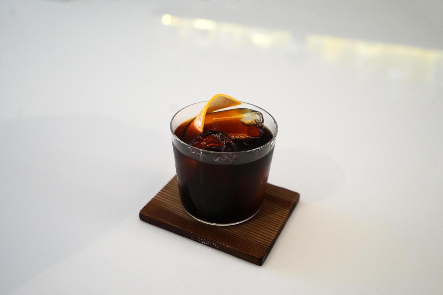 Close up glass of iced black coffee with slice of orange on wooden tray table photo