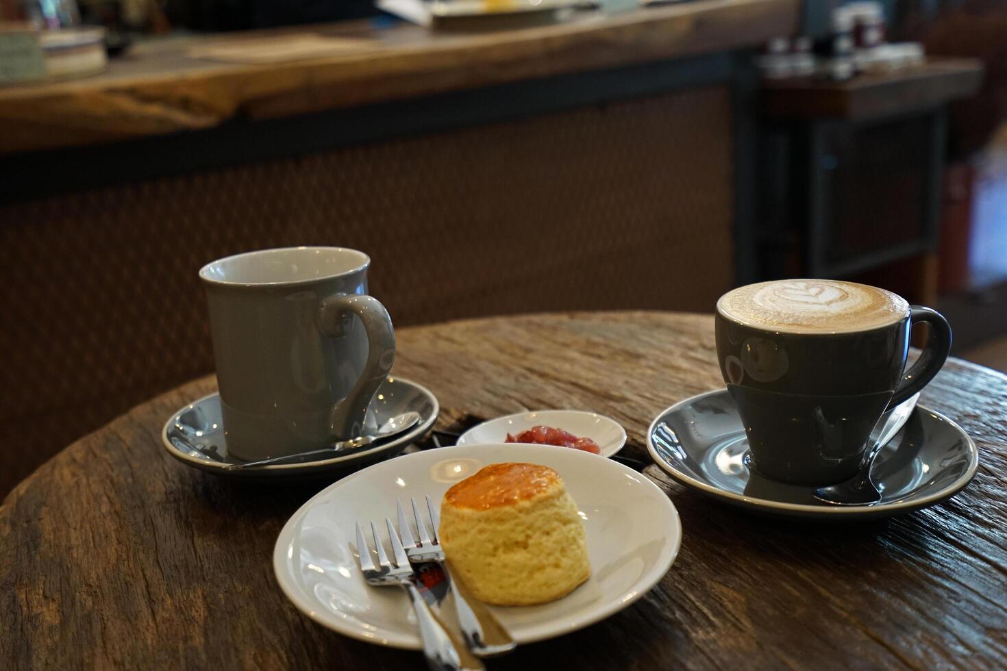 A ceramic cup of hot black coffee and Latte served with butter plain scone and berry jam on wooden table photo