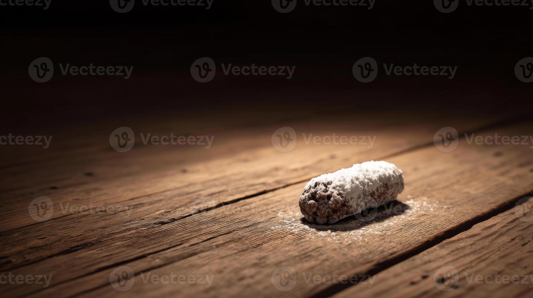 Single chocolate dessert roll dusted with powdered sugar on rustic wooden surface in dramatic lighting photo