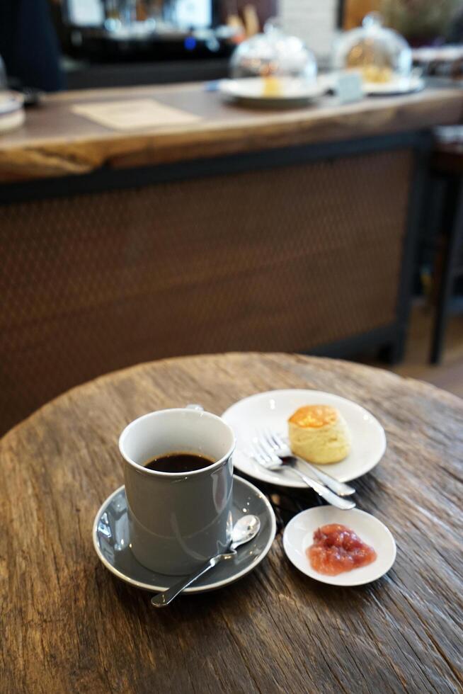 A porcelain cup of hot black coffee served with butter plain scone and berry jam on wooden table photo