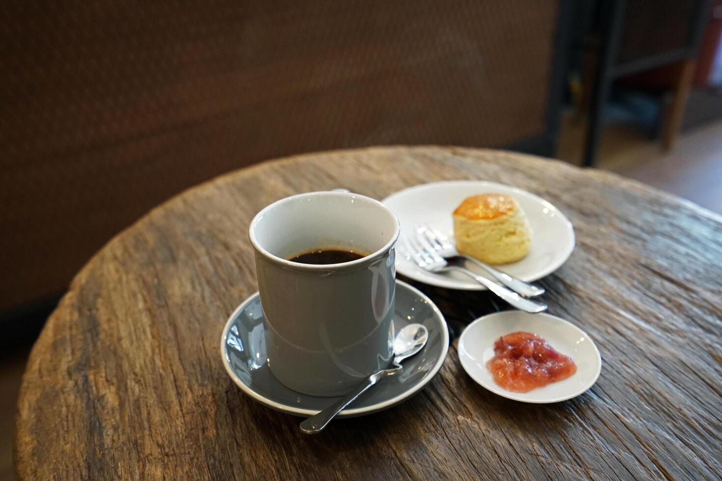 A ceramic cup of hot black coffee served with butter plain scone and berry jam on wooden table photo